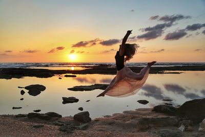 Woman jumping against sea during sunset