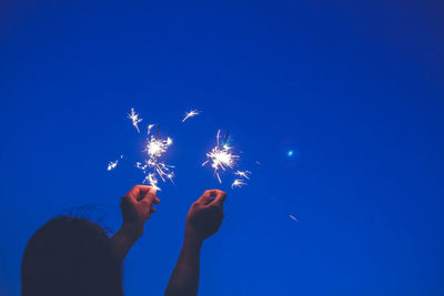 Rear view of woman holding sparklers against clear sky at night