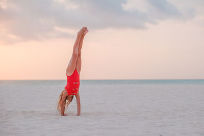 Woman with umbrella on beach against sky during sunset