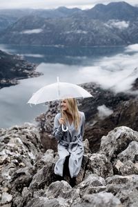 Woman standing with umbrella on rock by mountain
