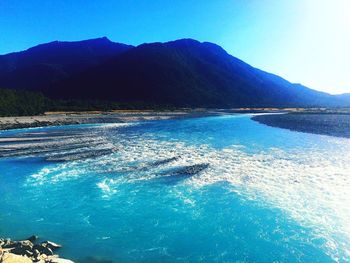 Scenic view of sea and mountains against clear blue sky