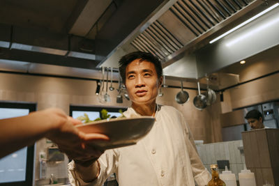 Male chef passing salad bowl to coworker working in commercial kitchen