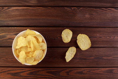 Cheese and chive potato crisp snack in brown bowl on wooden background top view