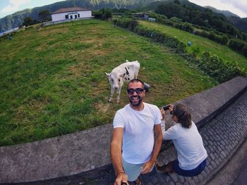 High angle view of happy man by woman photographing cow on field