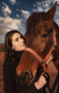 Young woman with horse against cloudy sky