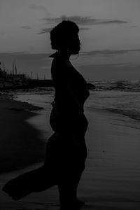 Silhouette woman standing on beach against sky during sunset