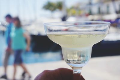 Close-up of hand holding drink at harbor against sky