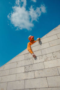 Low angle view of man standing by retaining wall against blue sky