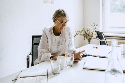Mature businesswoman using smart phone while sitting at desk in office