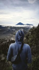 Rear view of man standing on mountain against sky