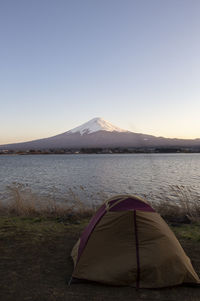 Tent on mountain by lake against clear sky