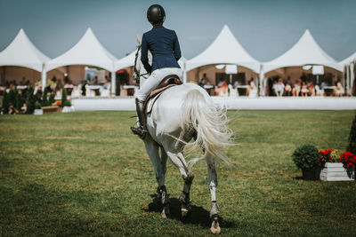 Rear view of woman riding horse against tents