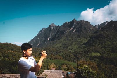 Side view of man photographing on mountain against sky