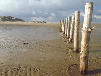 Wooden posts on beach against cloudy sky