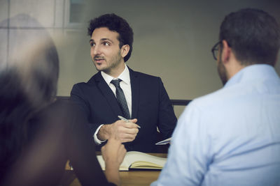 Young male businessman sitting with colleagues during meeting at law firm