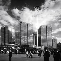 People on street by modern buildings against sky