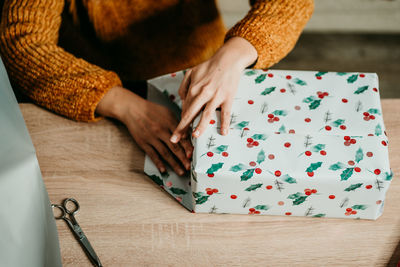 Midsection of woman wrapping christmas gift by table