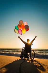 Man with balloons at beach against sky during sunset