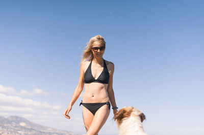 Woman in bikini with dog at beach against blue sky