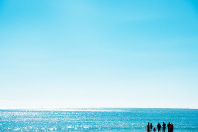 People at beach against clear blue sky