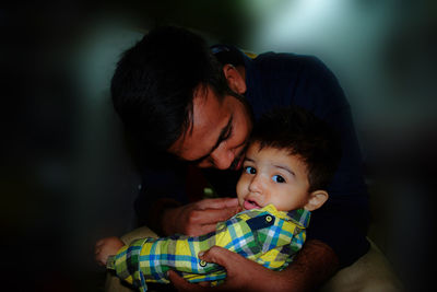 Father holding son while sitting at home