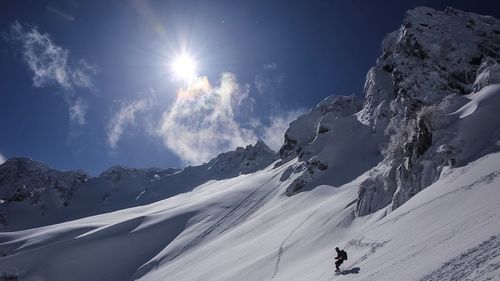 Man snowboarding on snow covered mountains against bright sky