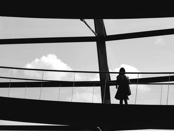 Rear view of woman standing by window against sky