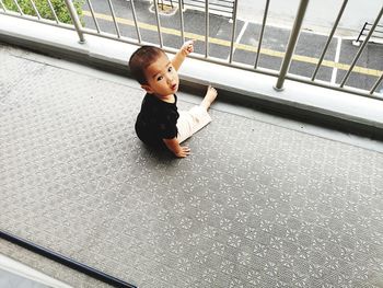 High angle view of boy sitting by railing and pointing at road