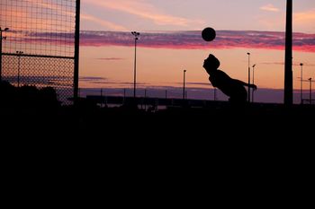 Silhouette man playing with soccer ball against sky during sunset