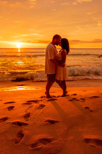 Rear view of couple standing at beach during sunset