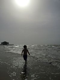 Silhouette boy running at beach against sky