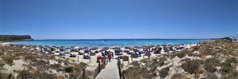 Panoramic view of people at beach against clear blue sky