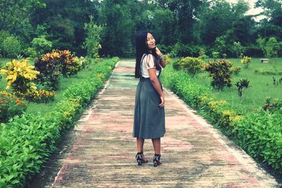 Portrait of young woman standing on footpath at park