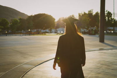 Rear view of silhouette woman walking on street against sky during sunset