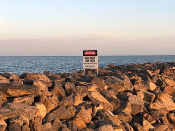 Sign on rock by sea against sky during sunset