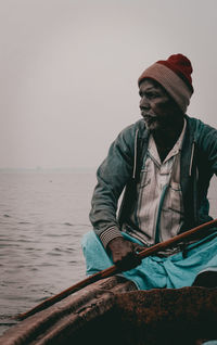 Man holding hat against sea against clear sky