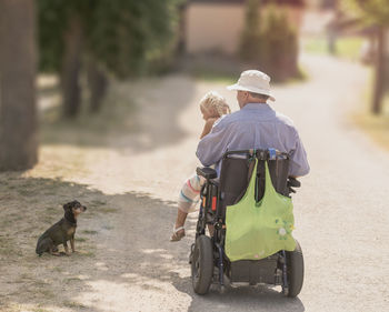 Rear view of granddaughter and grandfather sitting on wheelchair