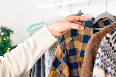 Woman's hand taking knitted sweater on hanger on clothes rack in shop with blurred christmas tree