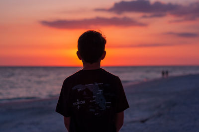 Rear view of man standing on beach during sunset