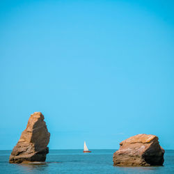 Rocks in sea against clear blue sky