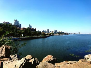 Scenic view of river by buildings against clear blue sky