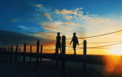 Silhouette people walking on pier at beach against sky during sunset