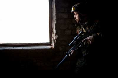 Young soldiers with guns, a soldier in equipment and with arms inspects a ruined house outside the