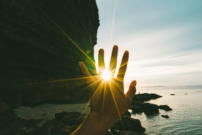 Sun shining over rocks by sea against sky