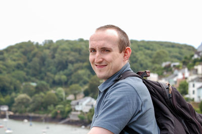 Portrait of happy man with backpack against clear sky