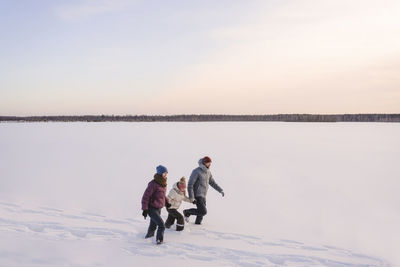 Family holding hands while walking on snow against sky during winter