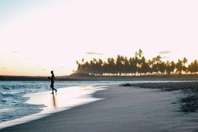 Man walking at beach against clear sky during sunset