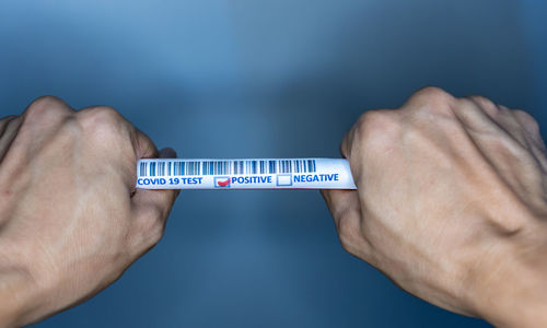 Close-up of hand holding paper against blue wall