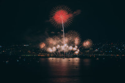 Firework display over illuminated city against sky at night