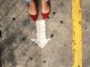 Low section of woman in red flat shoe standing in front of arrow sign on road